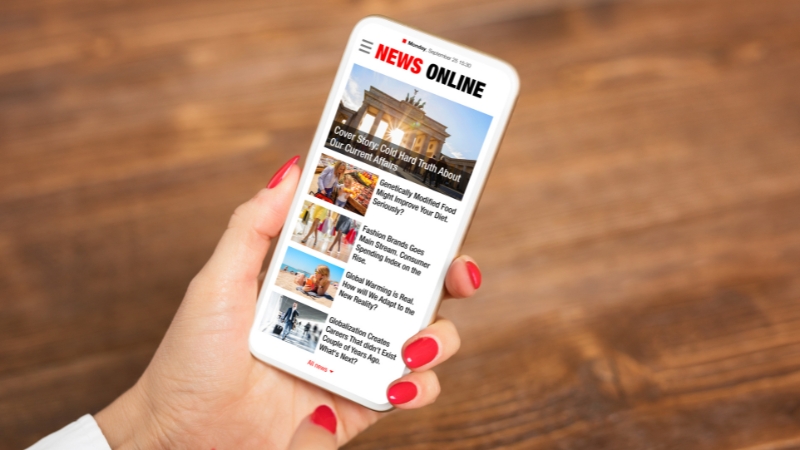 A person holds a phone and views a news website with images and headlines