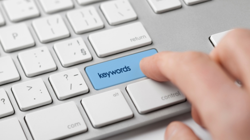 A person presses a keyboard button labeled keywords during keyword research