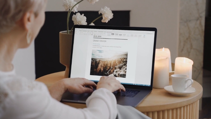 A woman works on a laptop in a cozy setting with candles and coffee beside her
